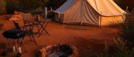Tienda de campaña montada en un entorno natural, con una hoguera y sillas de camping.