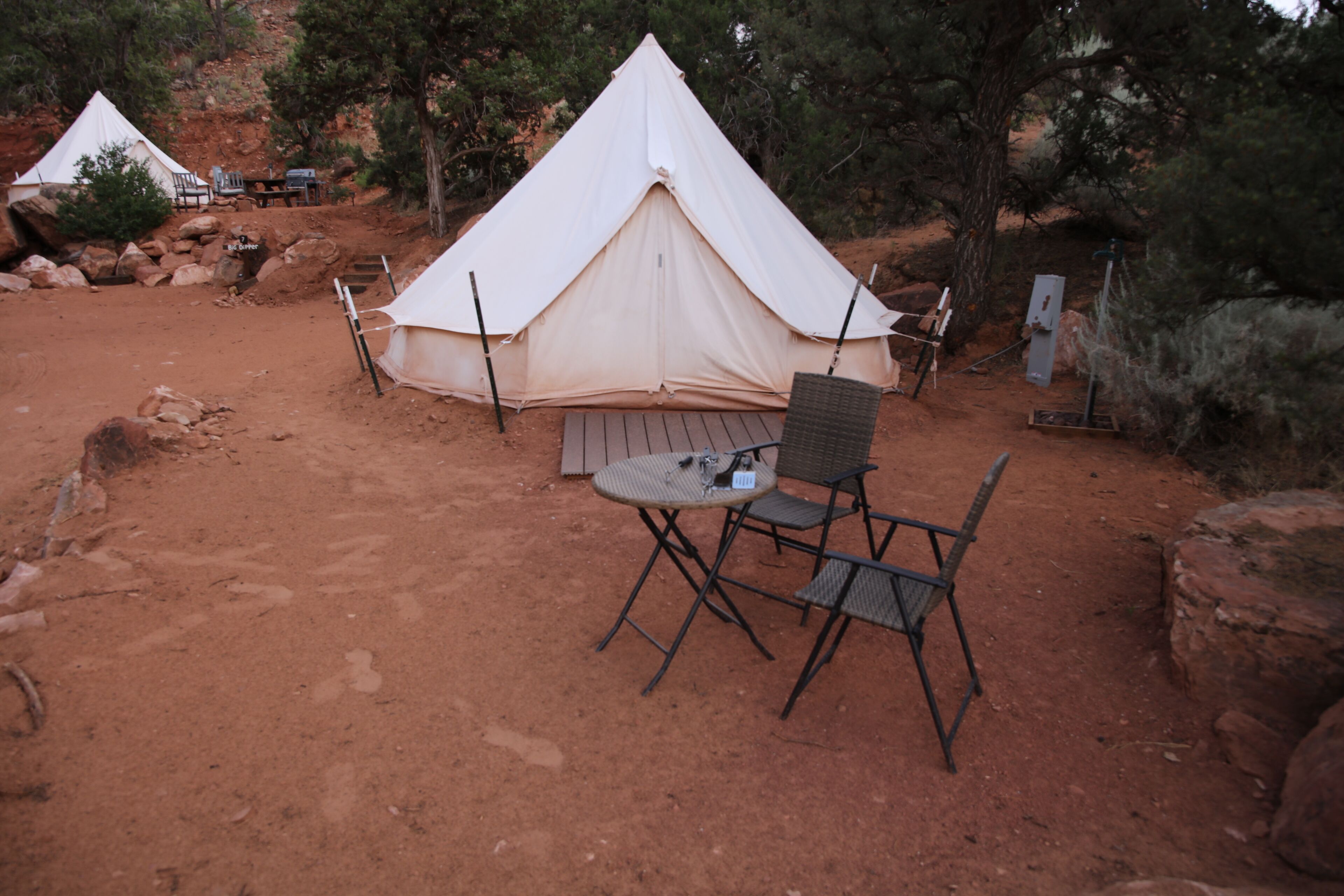 Un área de camping con tiendas de campaña, una mesa y sillas, rodeada de rocas y árboles.