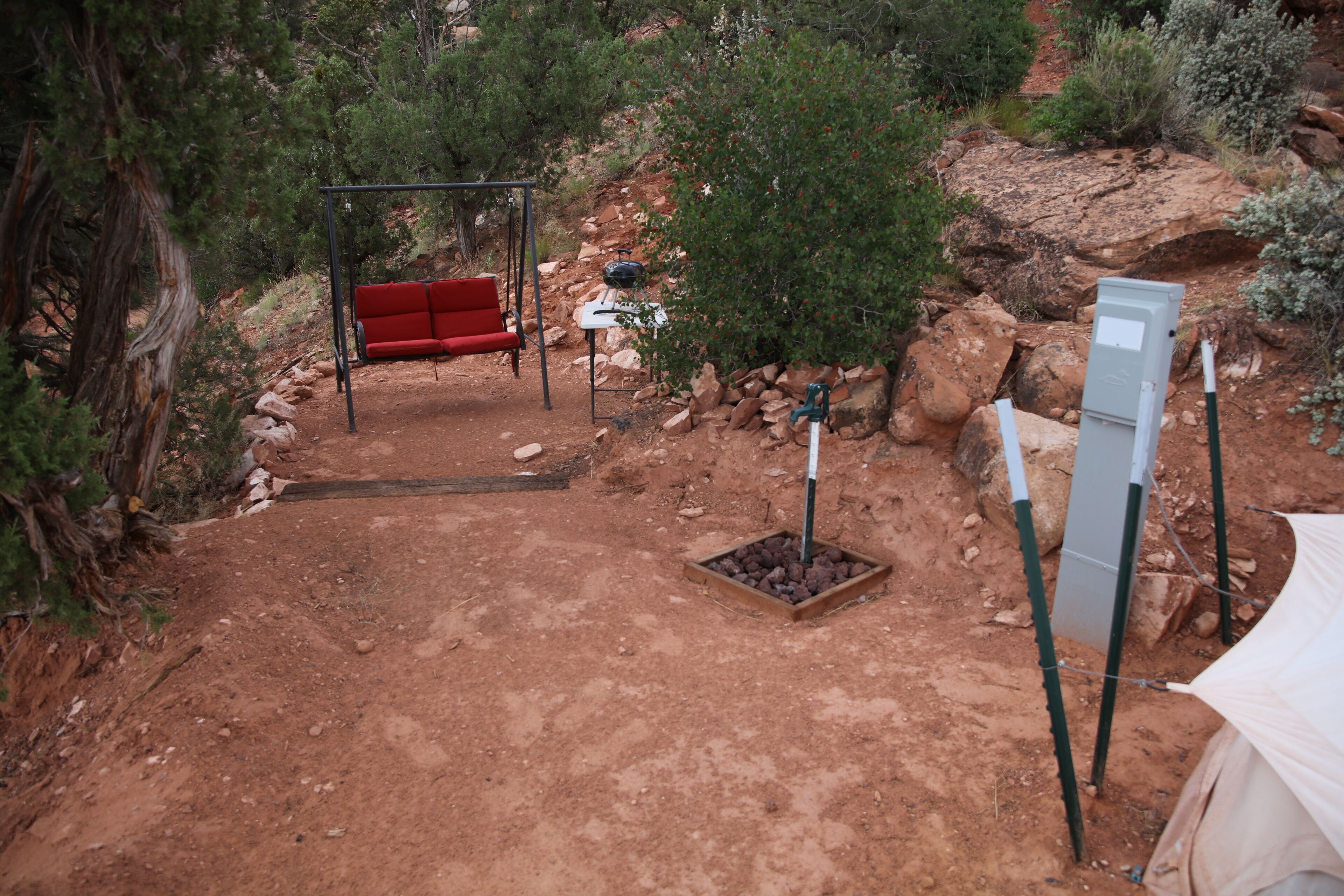 A dirt path leading to a red swing chair, a table with a kettle, and a tent in a natural setting.