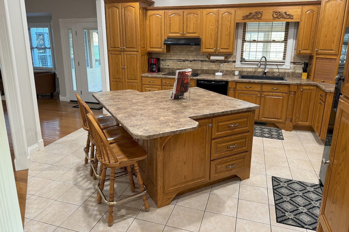 A kitchen with wooden cabinets, a granite countertop, and a built-in island with bar stools.