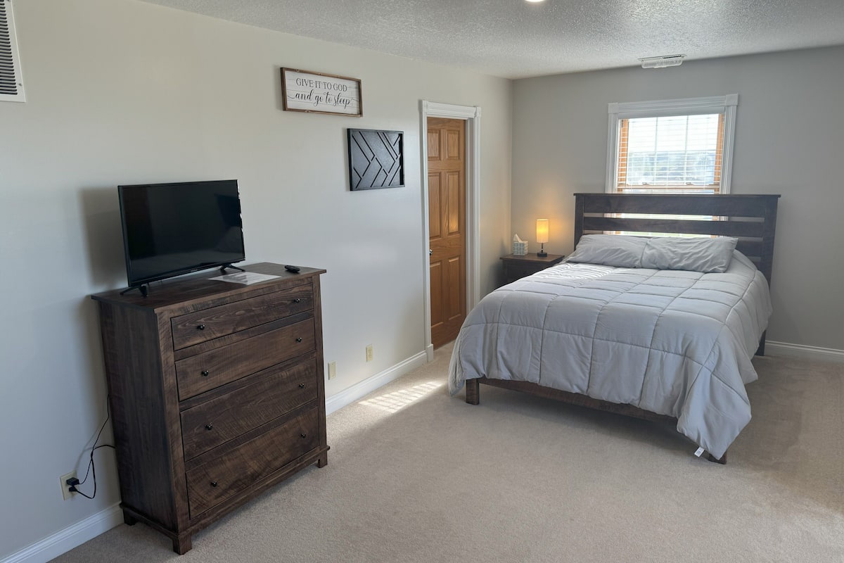 A bedroom with a bed, dresser, TV, and a motivational quote on the wall.