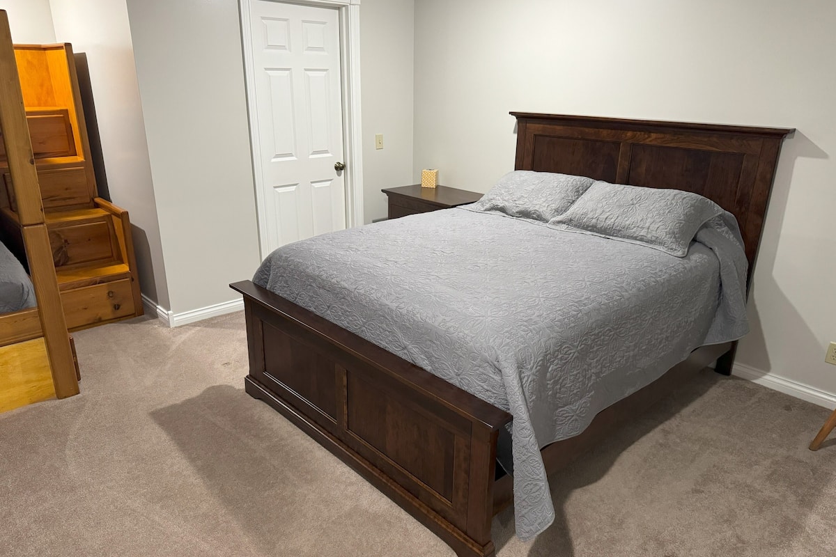 A bedroom with a wooden bed, a white door, a small nightstand, and a wooden ladder.