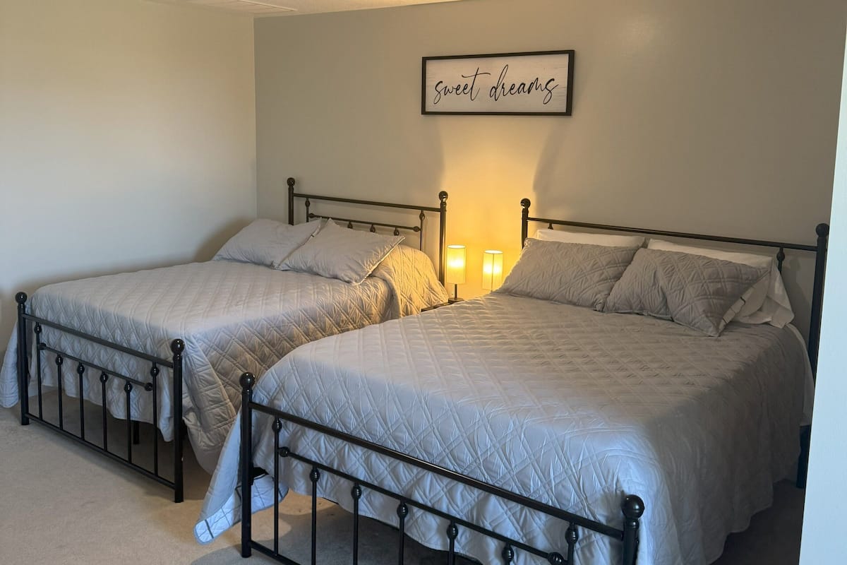 A bedroom with two beds, a ceiling light, and a wall sign that reads "sweet dreams".