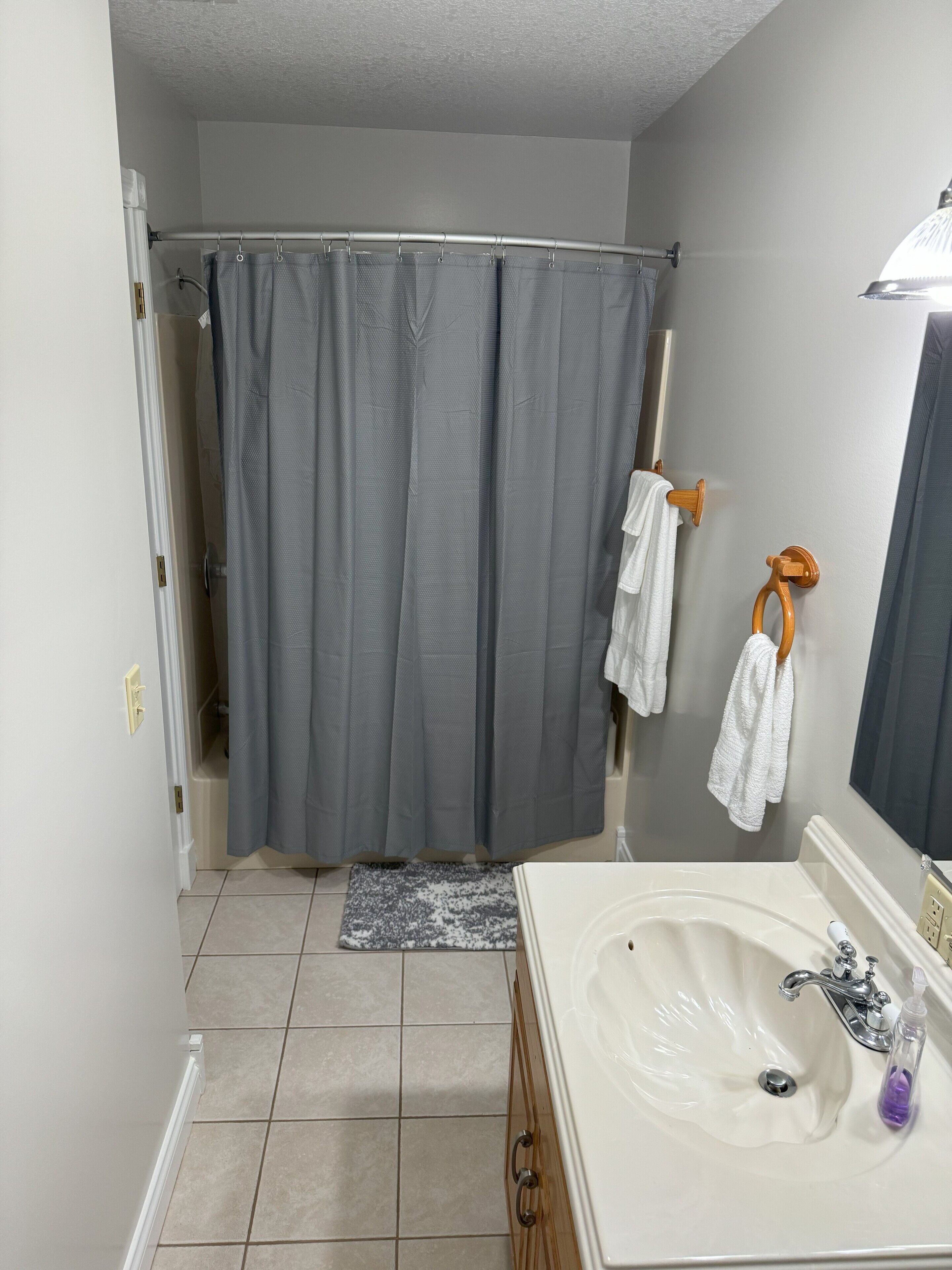 Une salle de bain avec un rideau de douche, un lavabo avec un miroir et un porte-serviettes.