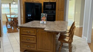 Una cocina con armarios de madera, encimera de granito, refrigerador, horno y microondas.
