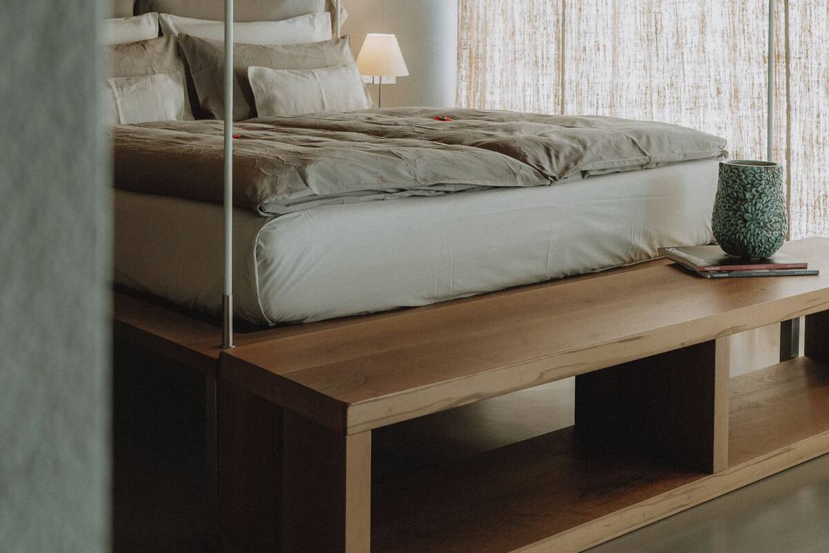 Quarto com teto de madeira, cama com várias almofadas, mesa de cabeceira e abajur.