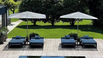 Zona de piscina con sillas de descanso y sombrillas, rodeada de vegetación y vistas a la montaña.