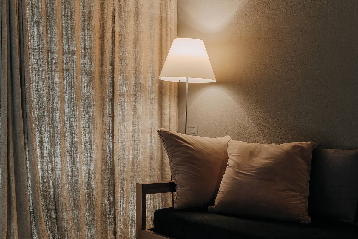 Um quarto aconchegante com teto de madeira, um sofá com almofadas, uma mesa com revistas e um abajur proporcionando iluminação suave.