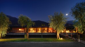A modern building with a glass facade, a bicycle parked outside, and a mountain in the background. - VIVERE suites and rooms (Arco)