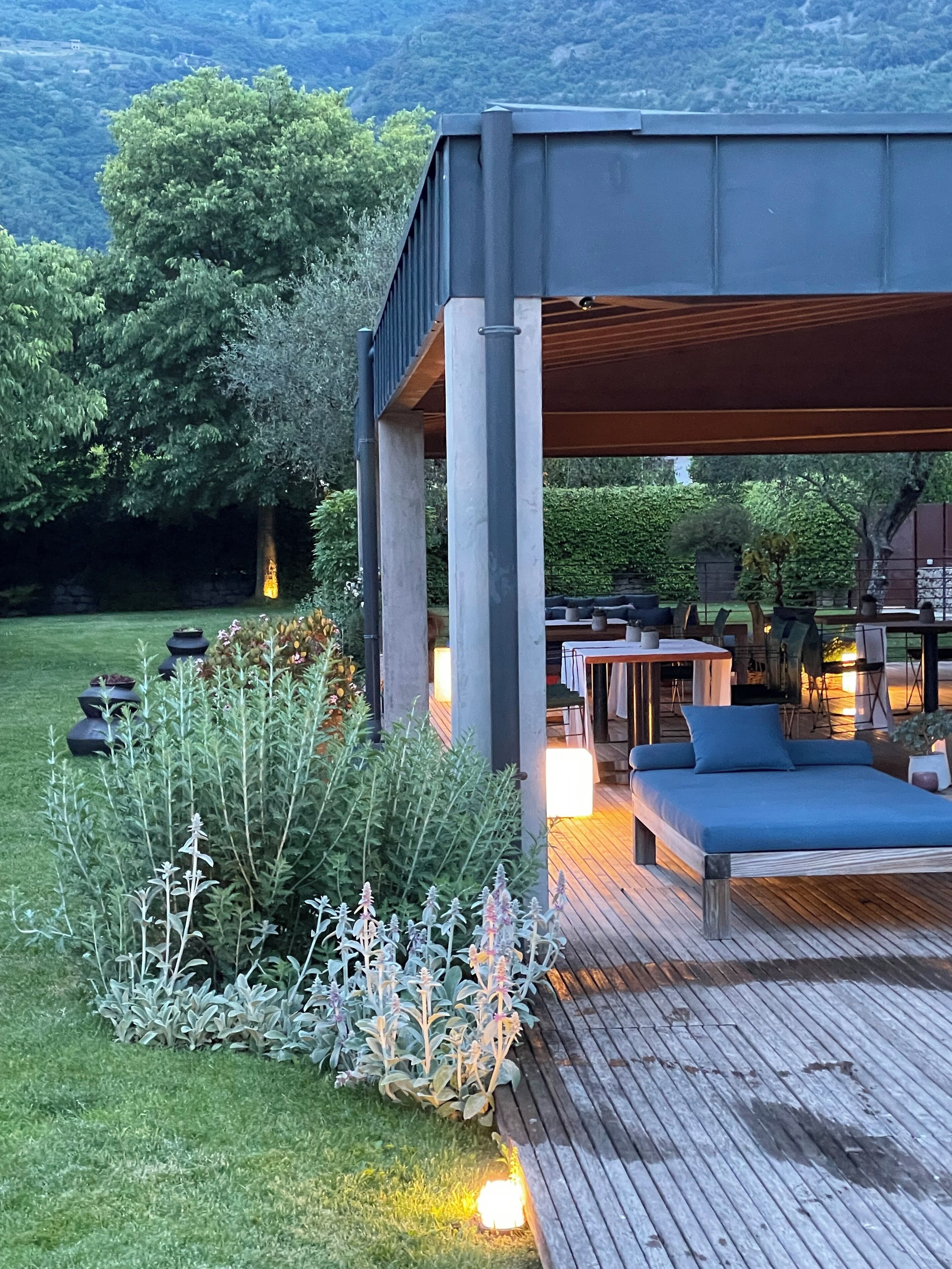 Une terrasse extérieure moderne, dotée d’un espace salon intégré, entourée d’une végétation luxuriante et offrant une vue sur un paysage montagneux.