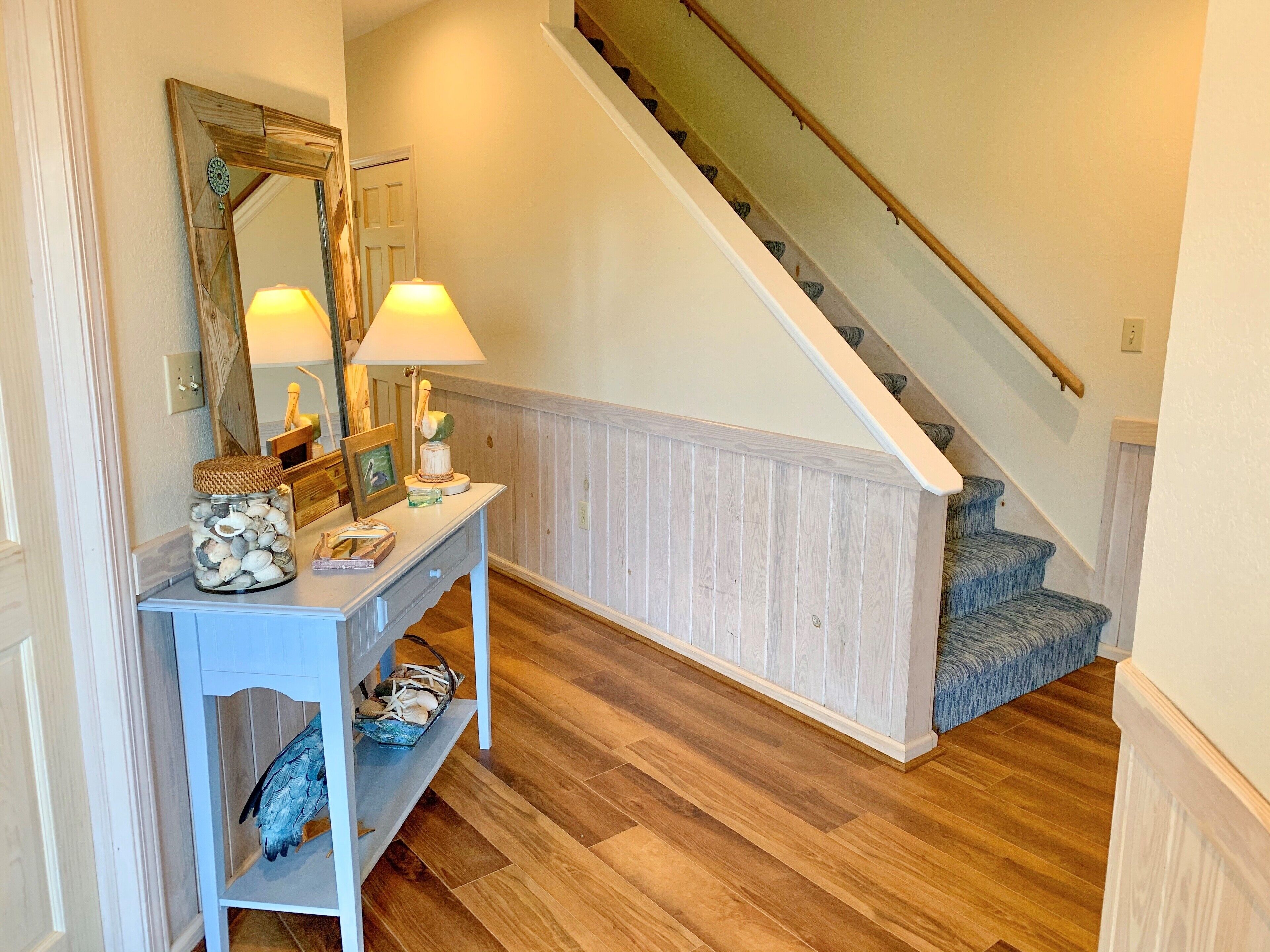 Un escalier avec des marches en bois et une rampe, menant à un palier où se trouvent une console blanche et un miroir.