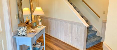 Un escalier avec des marches en bois et une rampe, menant à un palier où se trouvent une console blanche et un miroir.
