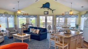 A spacious living room with a blue sofa, a dining area with white chairs, and a kitchen with a granite countertop. - Two If By Sea I and II: Larger home with fabulous views of Silver Lake (Ocracoke)