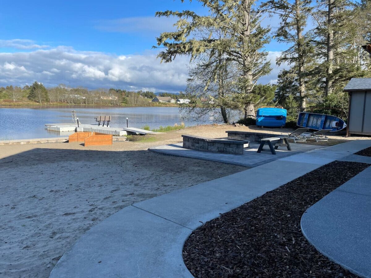 A lakeside park with concrete pathways, benches, and a picnic table.