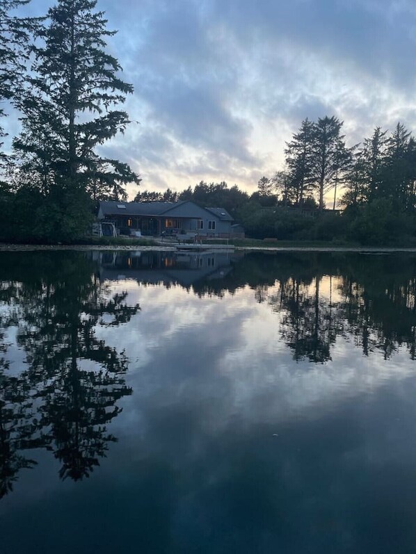A house with a dock extending into a calm lake, surrounded by trees.
