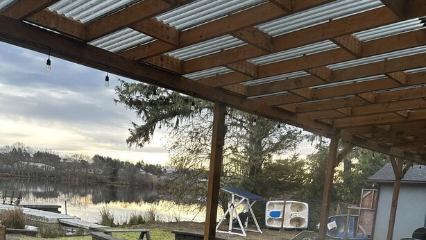 Área de hidromassagem externa com pérgola, emoldurada por paisagem natural e um corpo d'água.