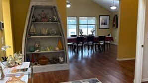 Uma área de refeições com uma mesa de madeira e cadeiras, um tapete e uma estante decorativa com diversos objetos.