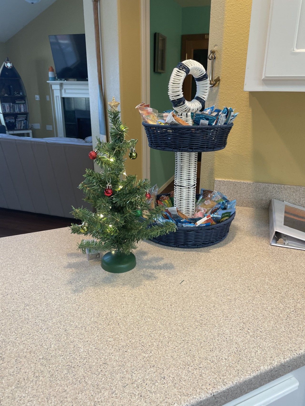 Una encimera de cocina con un pequeño árbol navideño, una cesta de mimbre y un armario blanco.