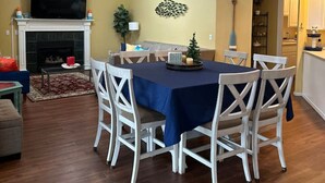 Uma sala de jantar com uma mesa posta para seis pessoas, cadeiras brancas, um ventilador de teto e uma lareira.