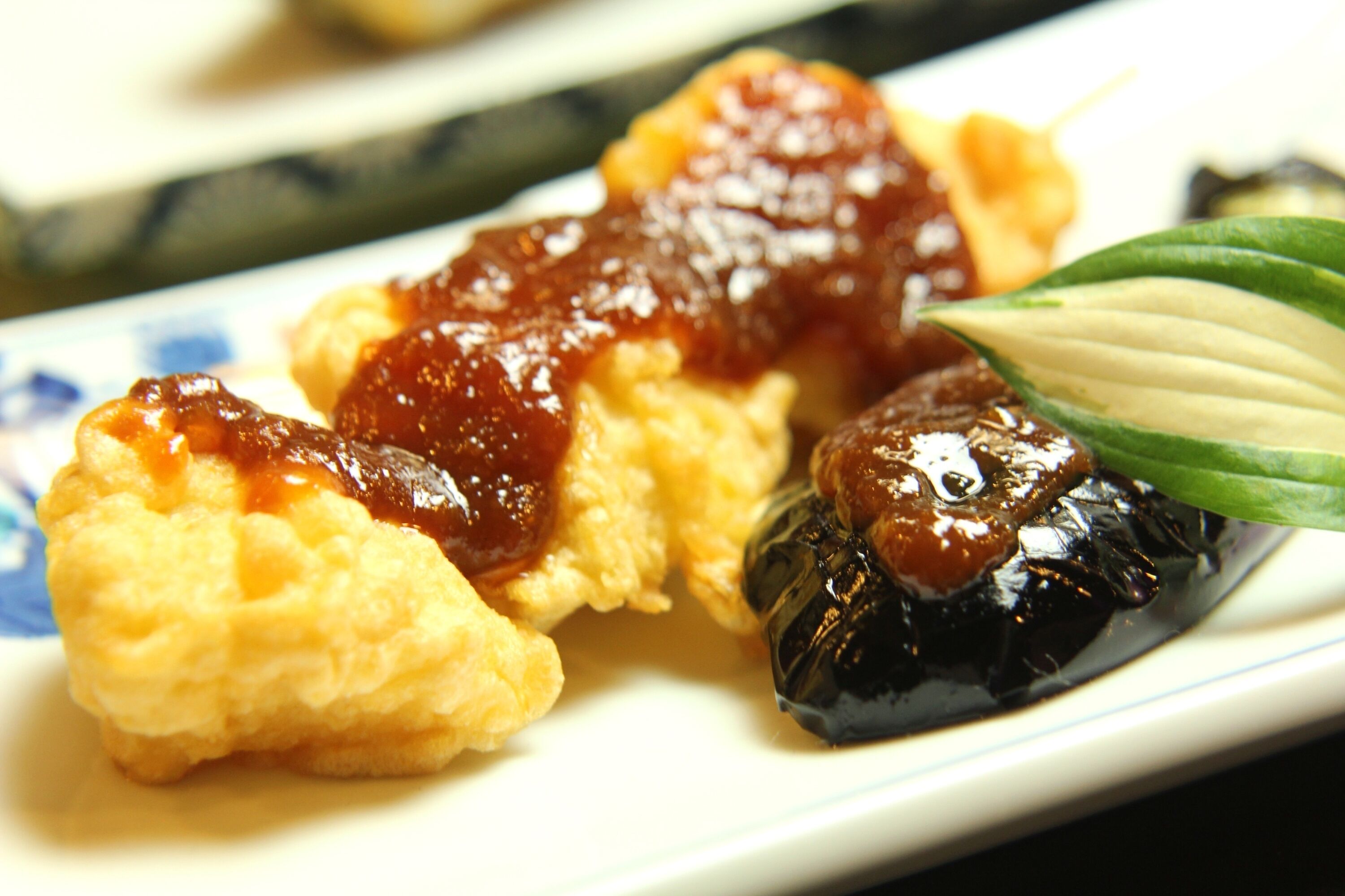 A plate with food items including a glazed meat and a green leaf garnish.