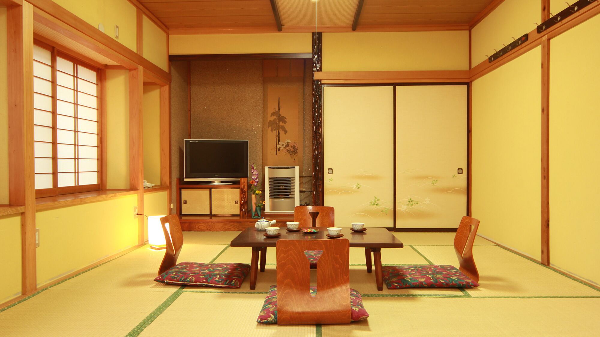 A traditional Japanese room with tatami flooring, a low table with cushions, a television, and a sliding door.