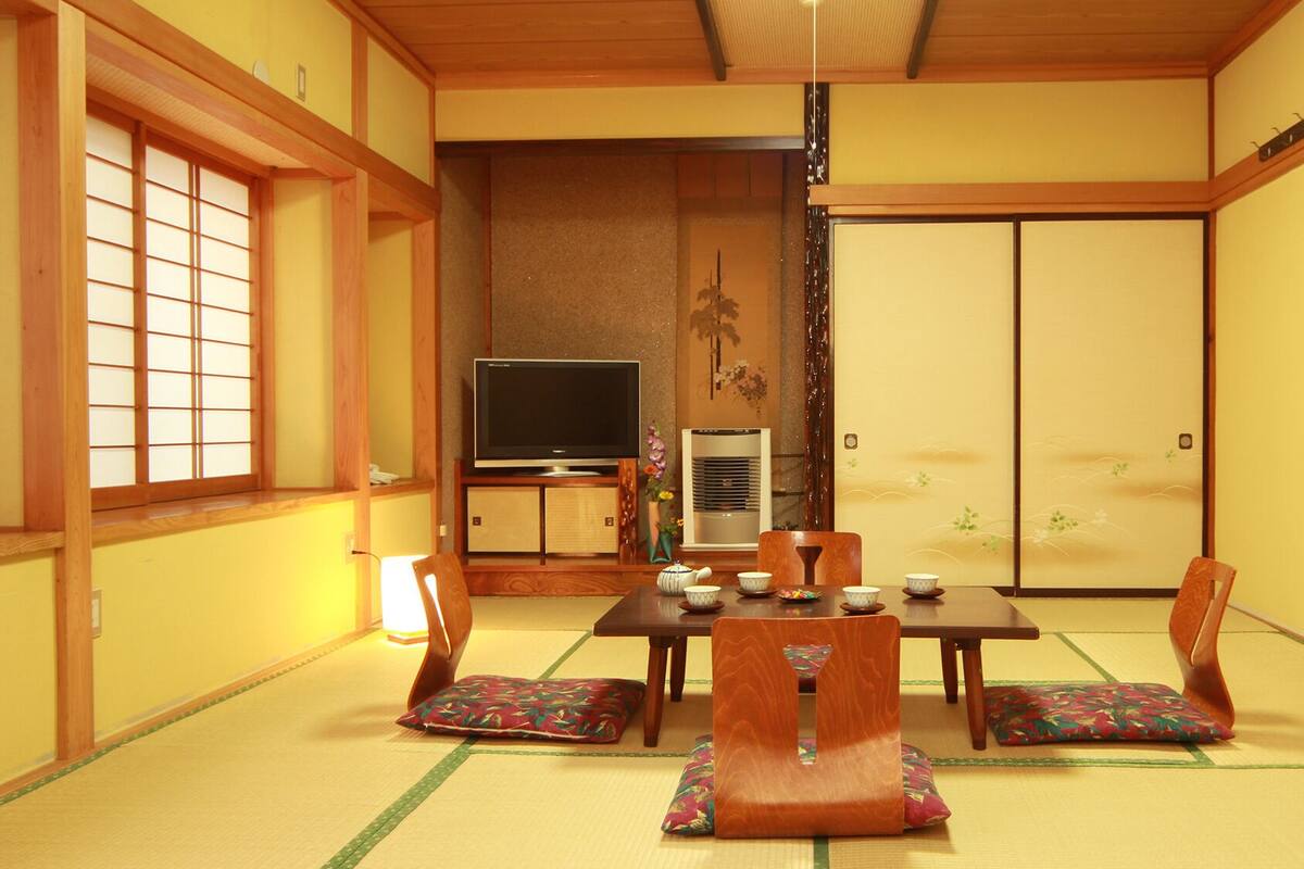 A traditional Japanese room with tatami flooring, a low table with cushions, a television, and a sliding door.