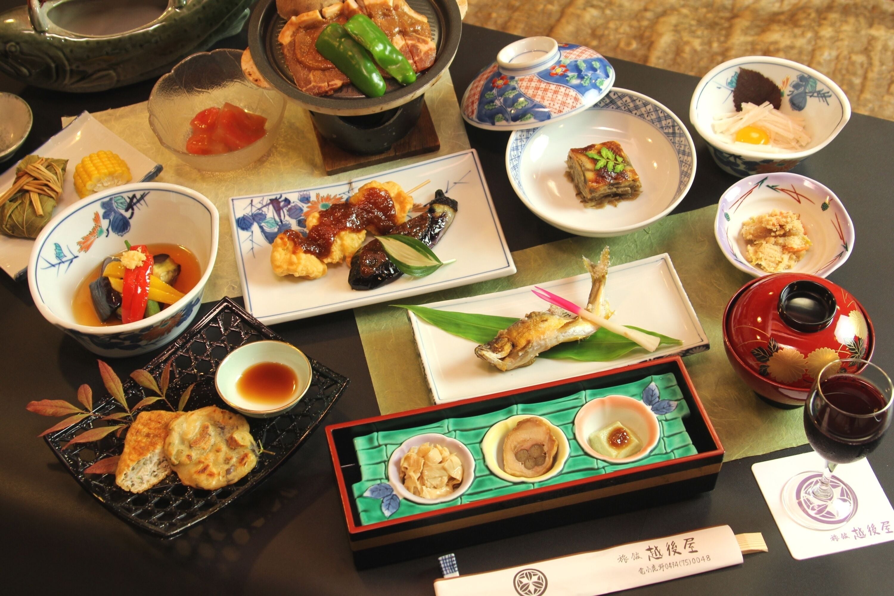 A variety of dishes and a glass of red wine on a table.