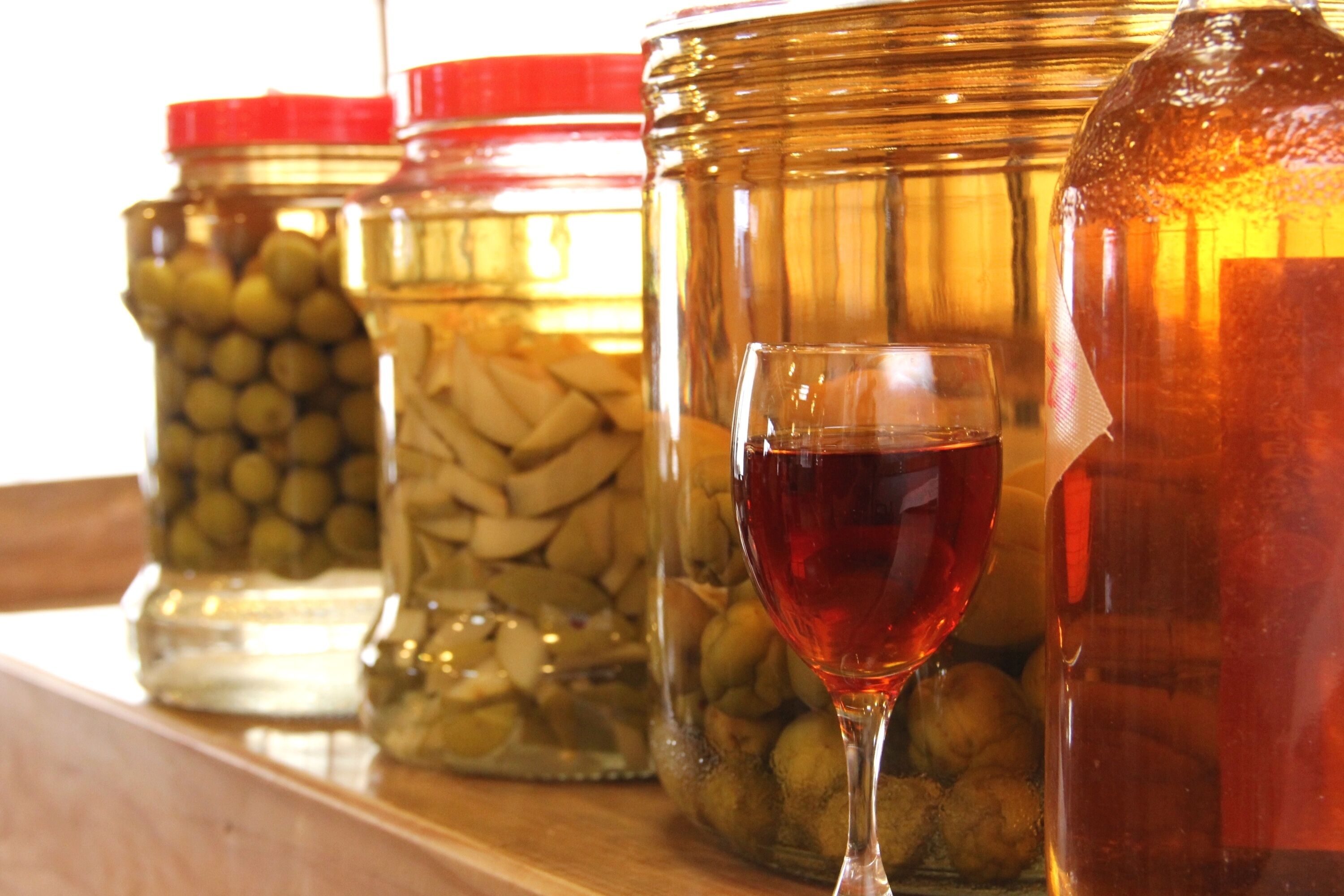 A shelf with jars containing olives, pickles, and a large jar of liquid.