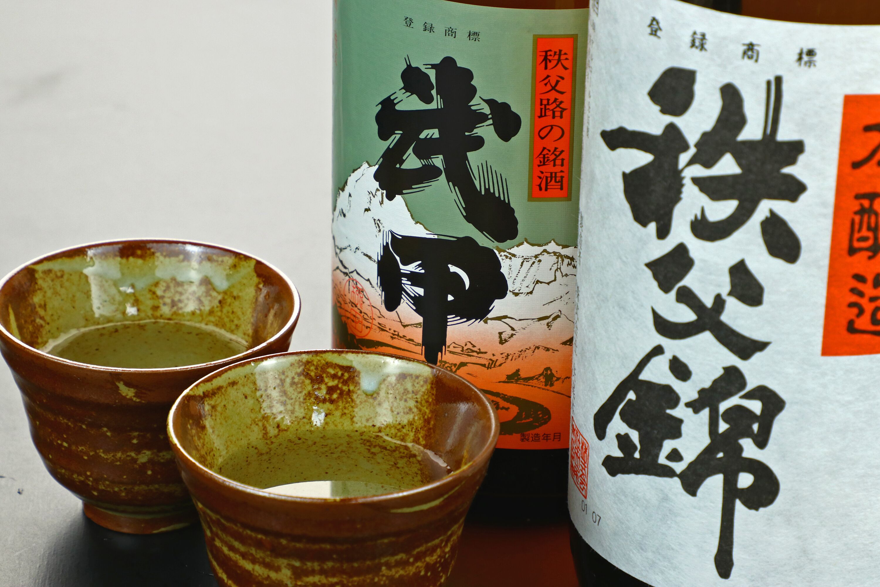 Twee keramische bekers en een fles met Japanse tekst.