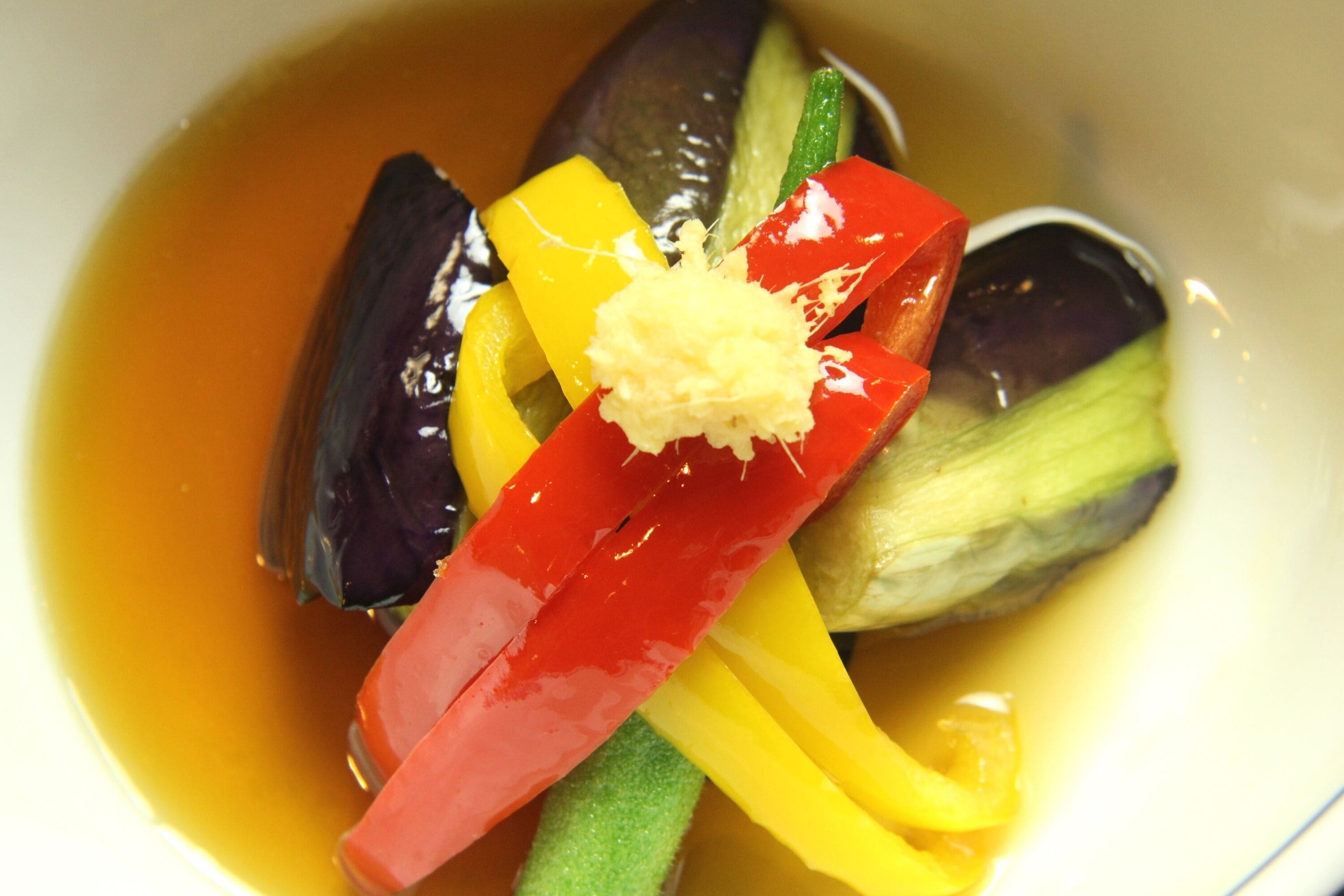 A bowl of soup with various vegetables and a piece of ginger.