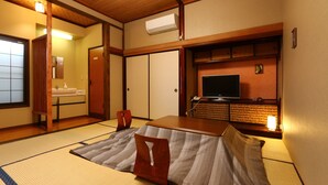 Une pièce de style japonais traditionnel, avec un sol recouvert de tatamis, une petite table en bois, un téléviseur et une porte coulissante.
