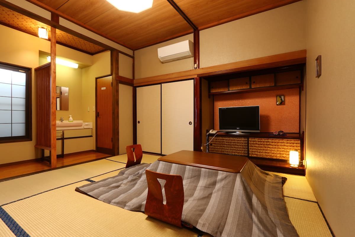 A traditional Japanese room with tatami flooring, a low wooden table, a television, and a sliding door.