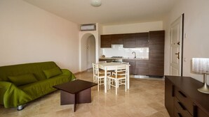 A compact living space with a green sofa, a small table, a dining area with chairs, a kitchenette, and a door. - Splendid Seaview Apartment (N° 20) (Porto Pozzo)