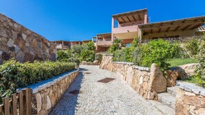 A stone pathway leading to a building with multiple balconies, surrounded by greenery and stone walls. - Splendid Seaview Apartment (N° 20) (Porto Pozzo)