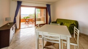A room with a dining table, chairs, a green sofa, a small cabinet, and a view of the outdoors through a sliding door. - Splendid Seaview Apartment (N° 20) (Porto Pozzo)