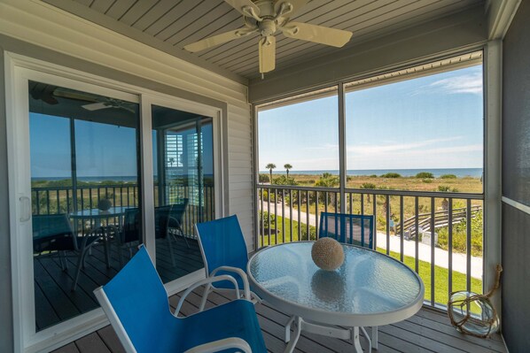 A covered outdoor area with a table and chairs, a ceiling fan, and a view of the beach.