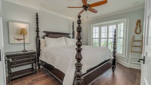 A bedroom with a four-poster bed, a ceiling fan, a nightstand with drawers, a lamp, and a window with blinds. - Spend some time in this gorgeous villa with a gorgeous view! B3623A (Cape Haze)