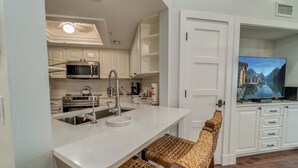 A modern kitchen with white cabinetry, a built-in microwave, a stainless steel sink, and a large flat-screen TV mounted on the wall. - Spend some time in this gorgeous villa with a gorgeous view! B3623A (Cape Haze)