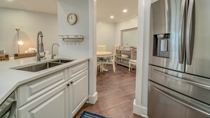A modern kitchen with white cabinetry, a stainless steel refrigerator, and a dining area with a wooden table and chairs. - Spend some time in this gorgeous villa with a gorgeous view! B3623A (Cape Haze)