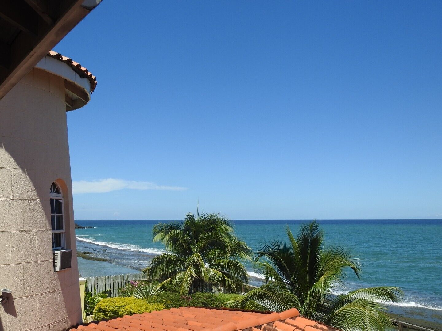 A coastal view with a building featuring a red-tiled roof and a clear blue sky.