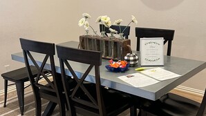 Ein Essbereich mit einem Tisch für vier Personen, mit einer Uhr, einer Blumenvase und einem Willkommen-Schild.
