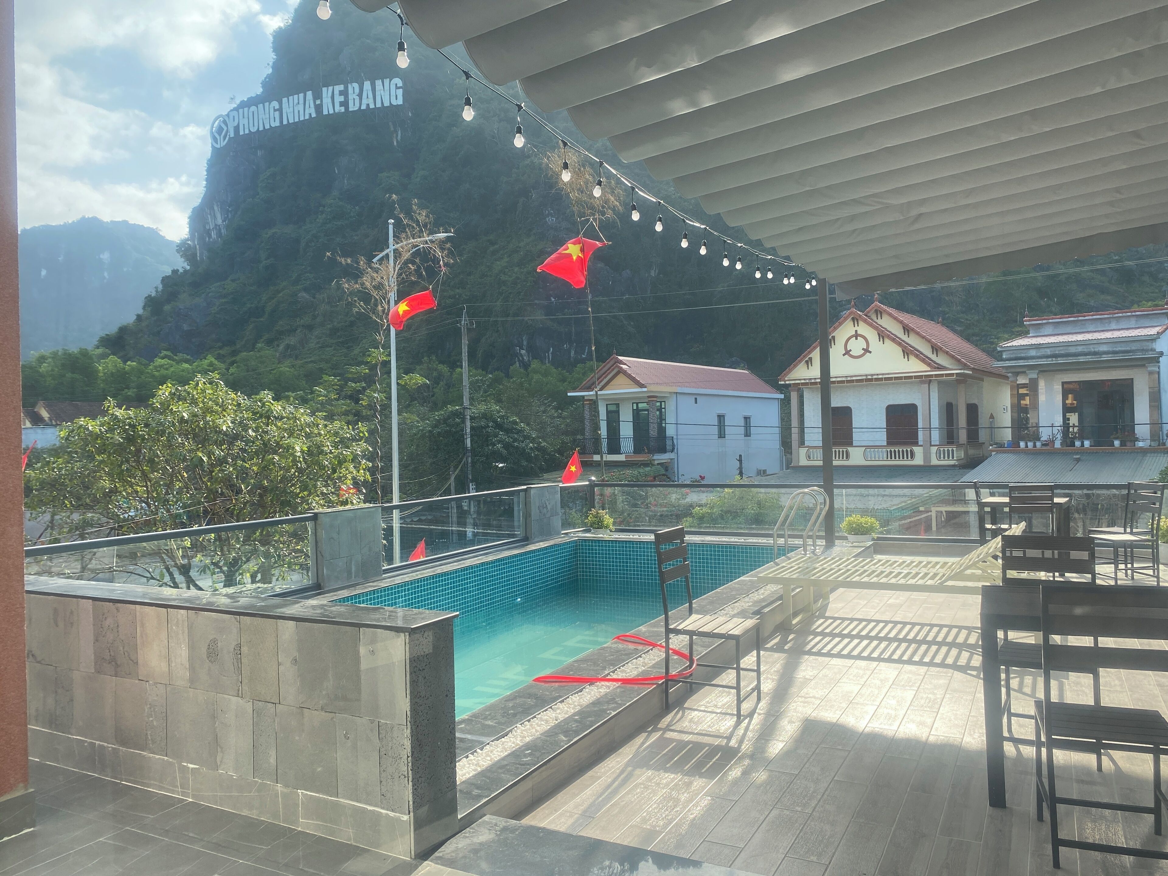 A pool area with a view of a mountain and a building with a sign reading "PHONG NHA-KE BANG".