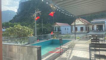 A pool area with a view of a mountain and a building with a sign reading "PHONG NHA-KE BANG".