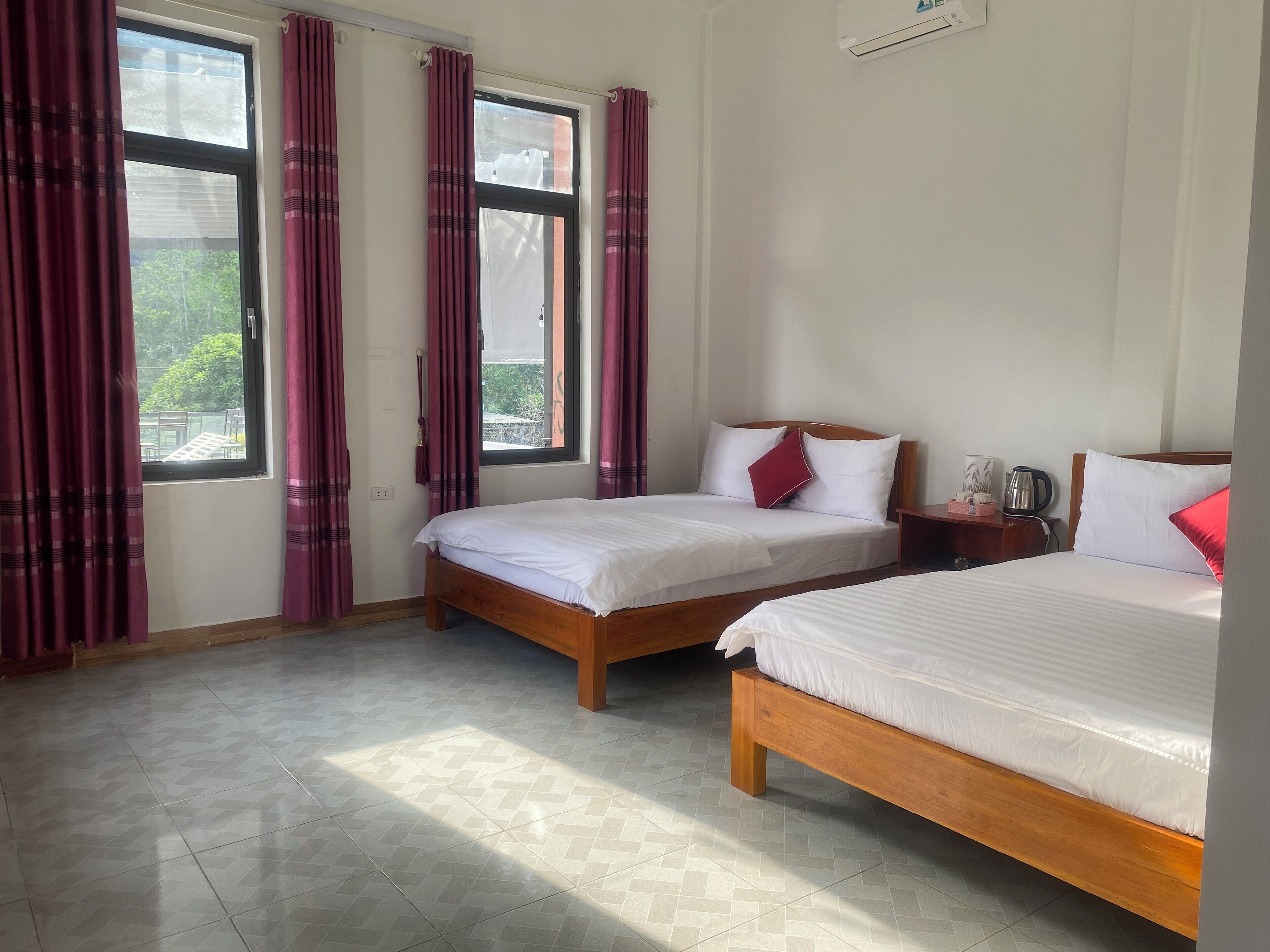 A hotel room with two beds, a wooden headboard, a nightstand, and a window with curtains.