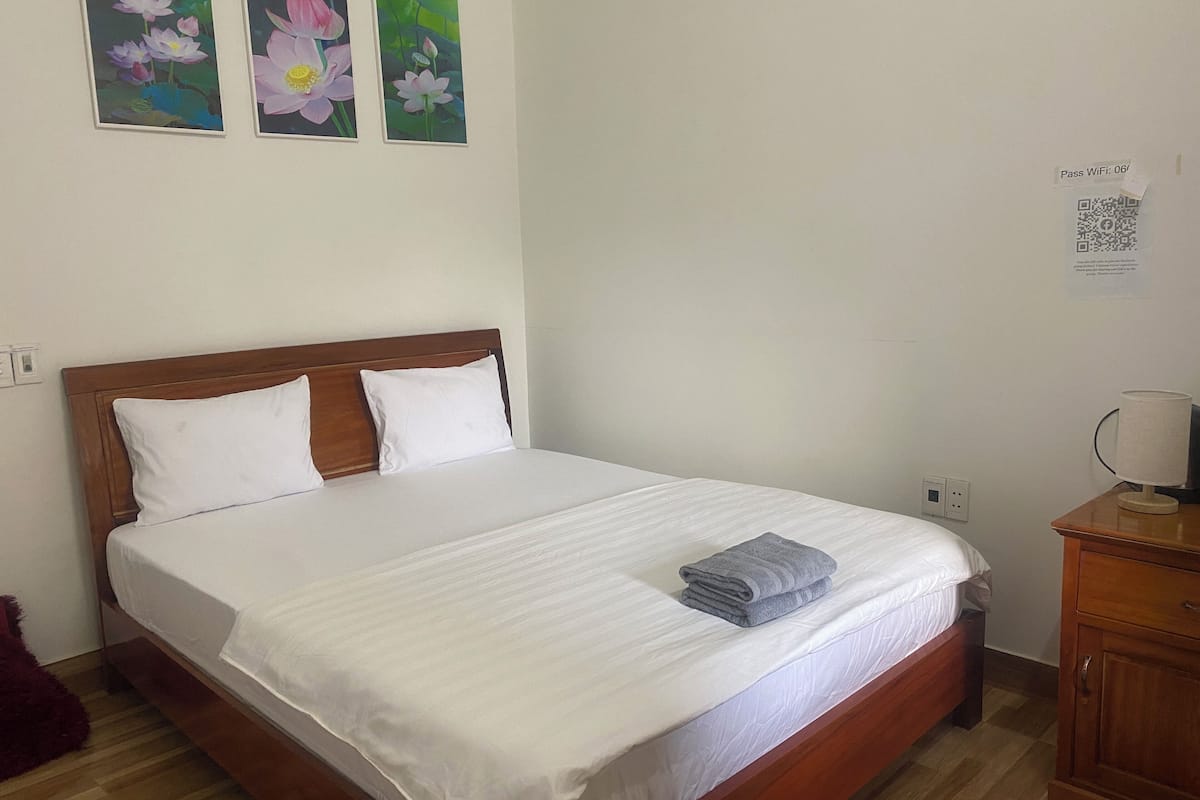 A neatly made bed with white linens, a wooden headboard, and a folded towel on the foot of the bed. There are three framed floral paintings on the wall above the bed.