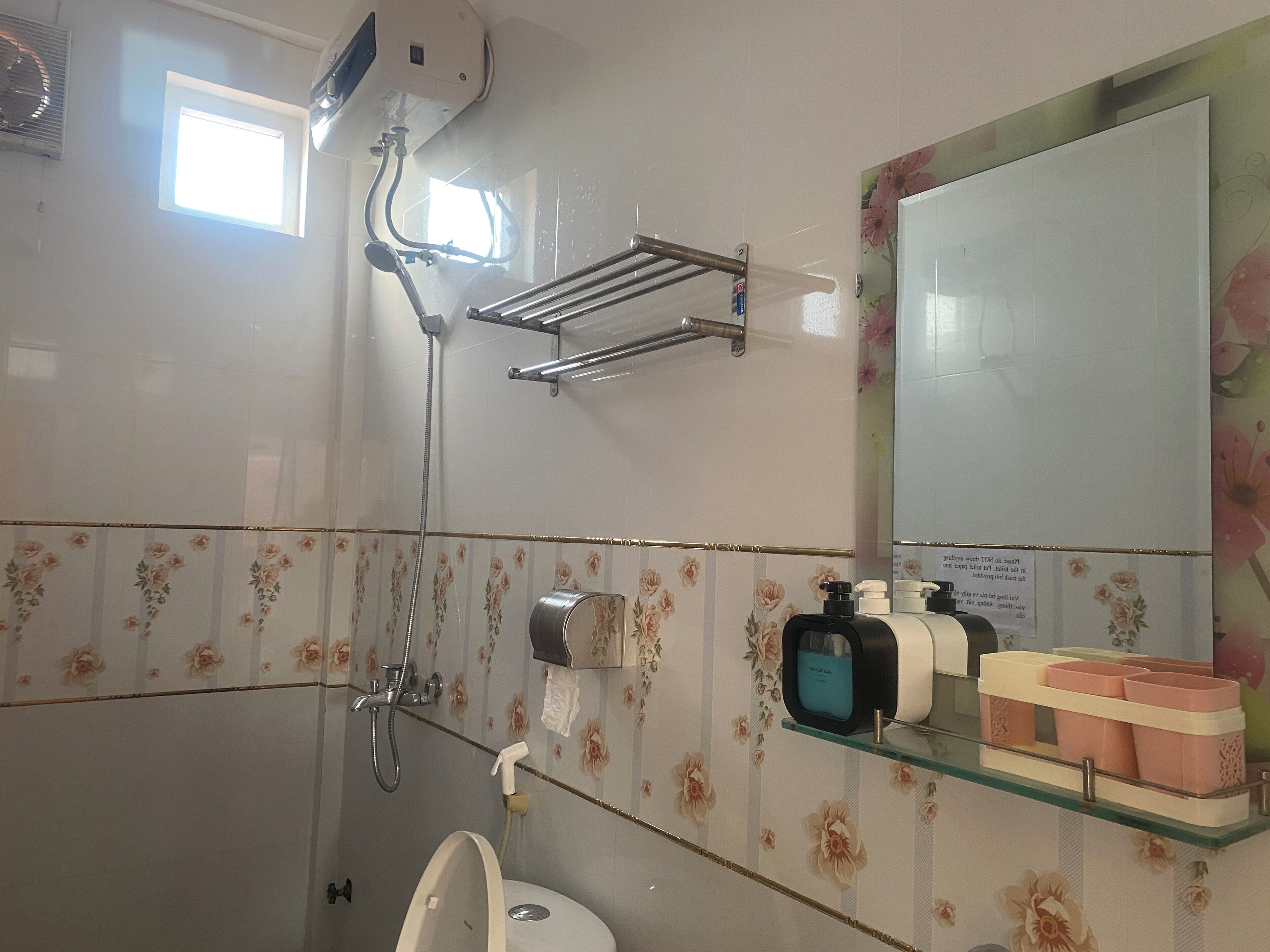 A bathroom with a shower, a toilet, a sink, a mirror, and a shelf with toiletries.