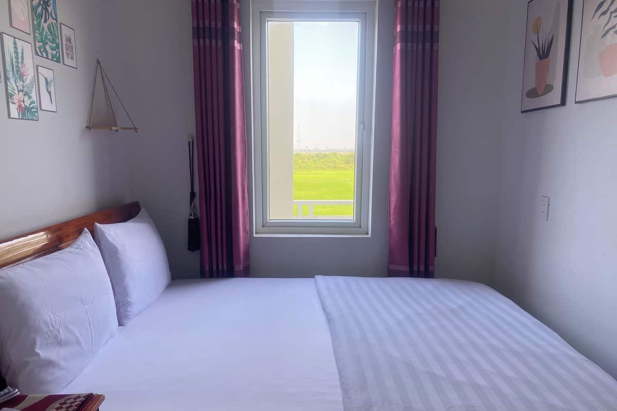 A neatly made bed with white linens, a wooden headboard, and a bedside table with a red and white checkered tablecloth.
