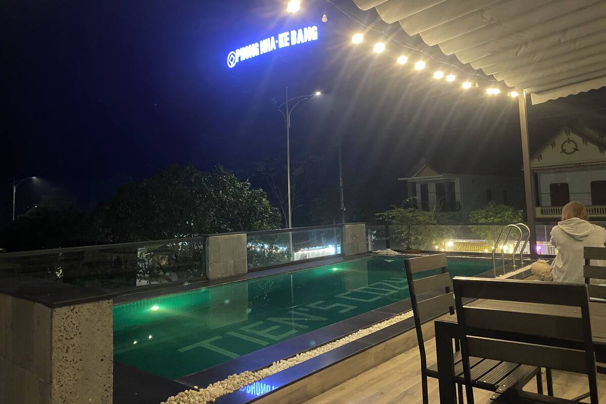 An outdoor pool area with a sign reading "PHONG NHIA - KE BANG" and a person sitting on a bench.