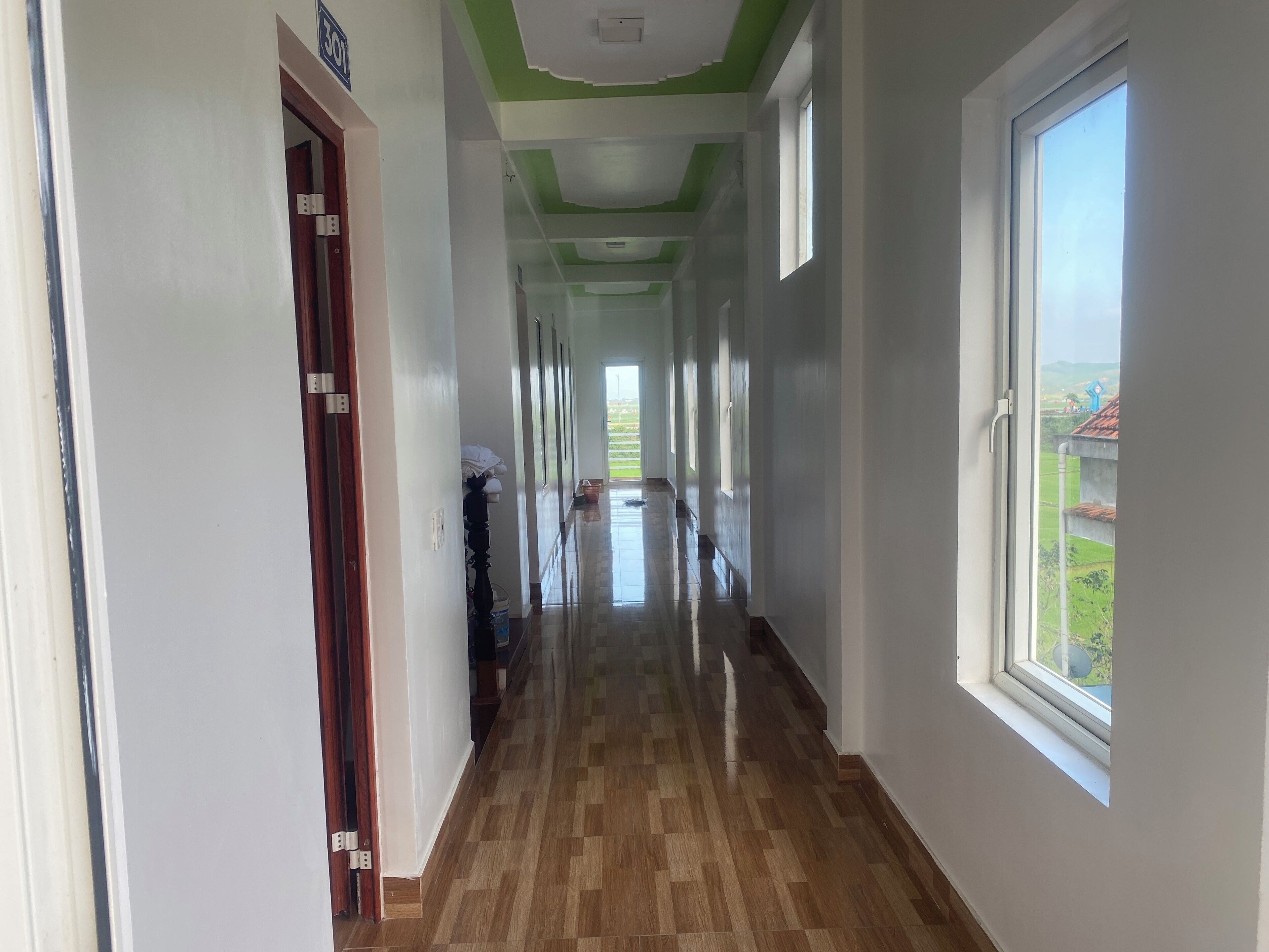 Ein Flur mit Holzboden, weißen Wänden und einer grünen Decke. Rechts befinden sich Fenster und links eine Tür.