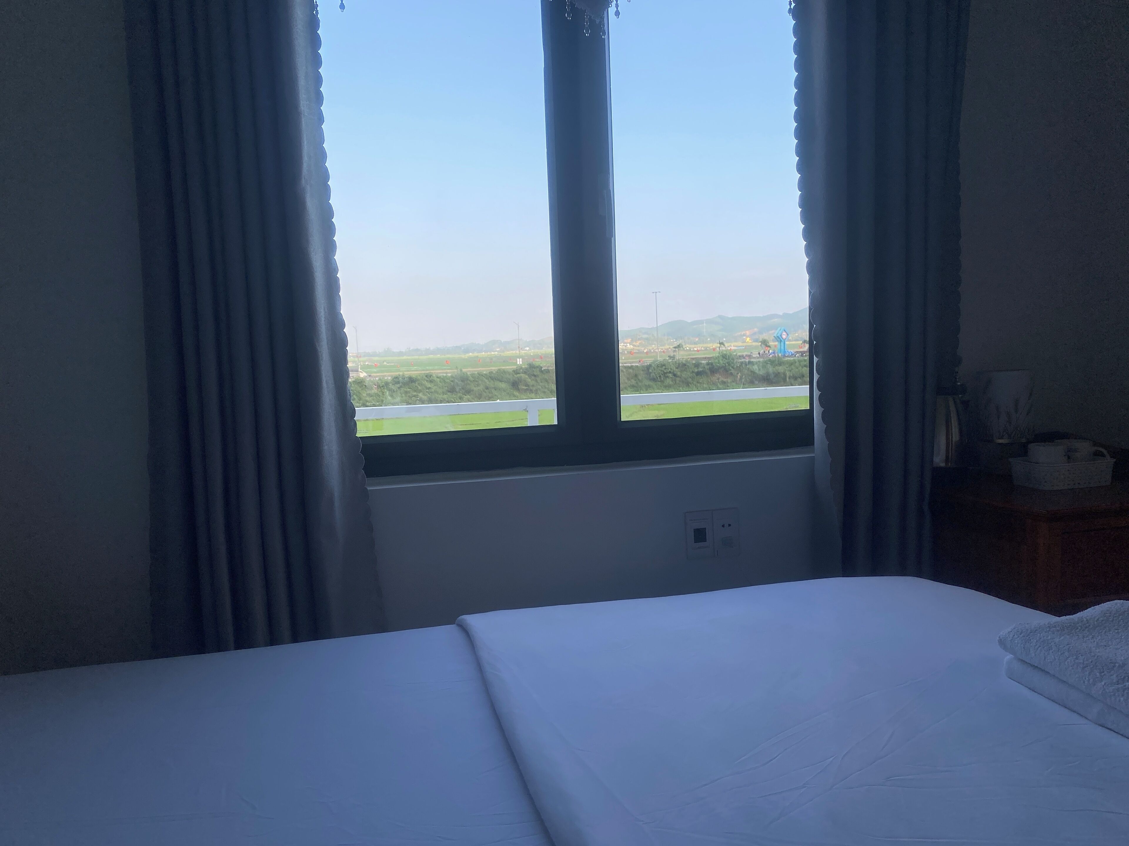 Een hotelkamer met een bed, een raam met gordijnen en uitzicht op een groen landschap.